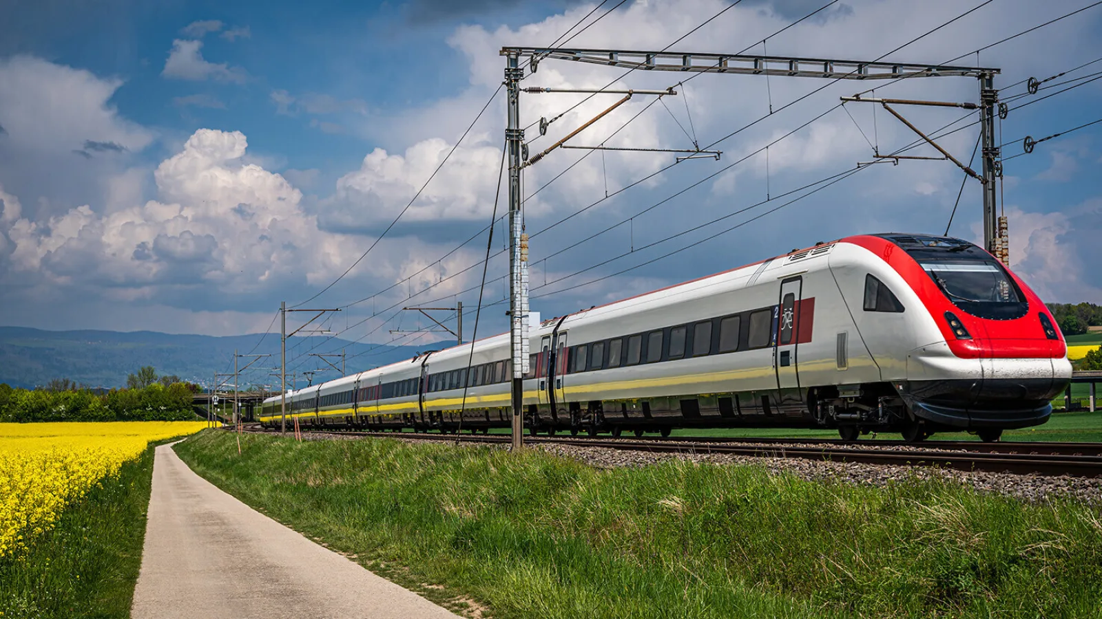 Train running through rapeseed field in spring. Red train, railroad with blue sky, yellow flowers and green field. Chavornay, Switzerland.